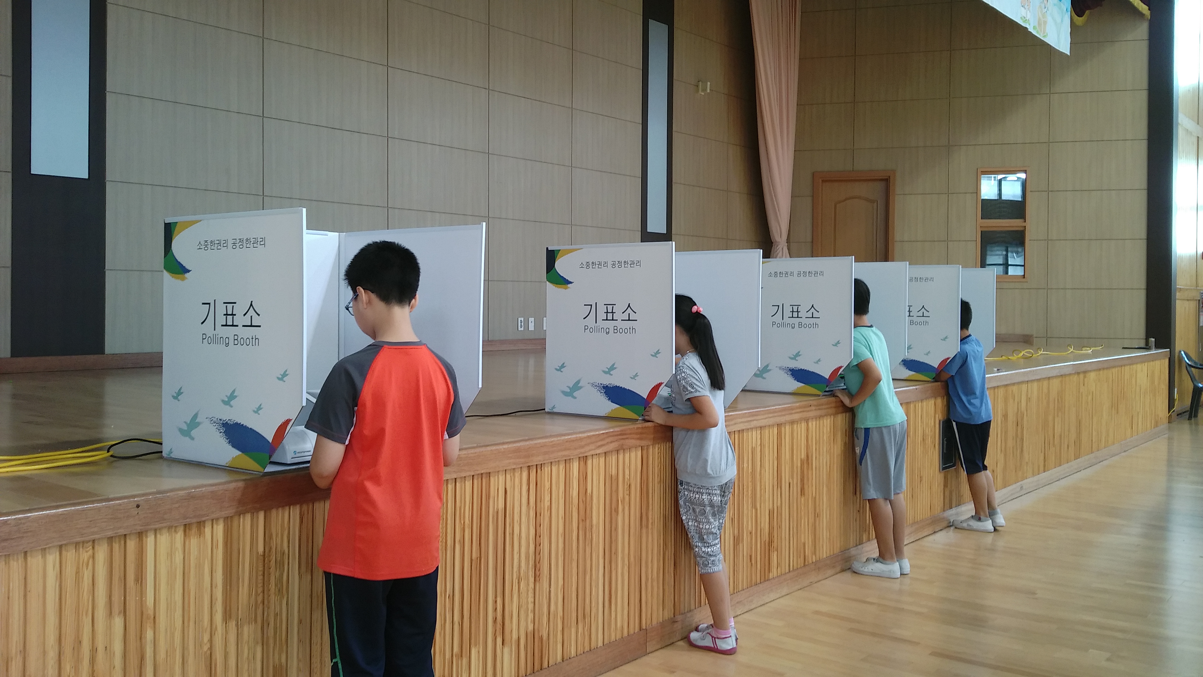 4개의 기표소에서 각각 4명의 학생들이 투표를 하고 있는 모습